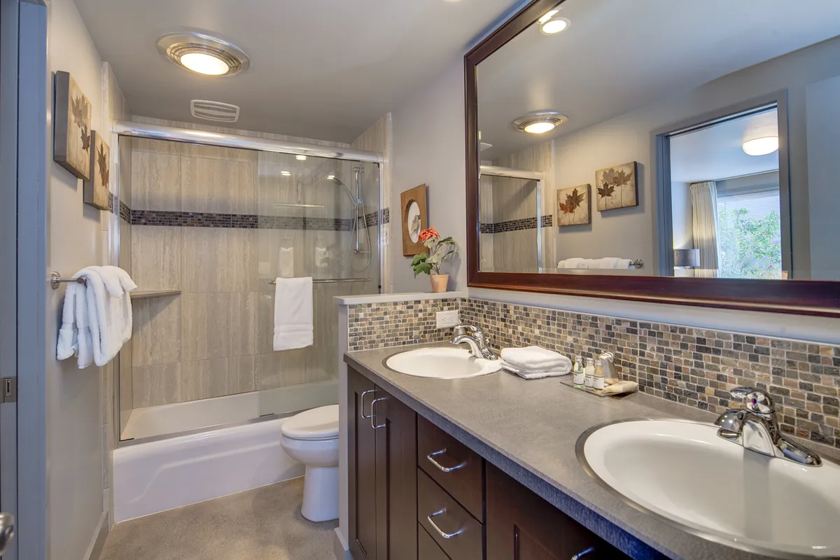 A modern bathroom with a double sink vanity, glass shower enclosure, tasteful wall art, and a large mirror reflecting soft natural light. The space feels tranquil and well-appointed for both morning routines and evening relaxation.