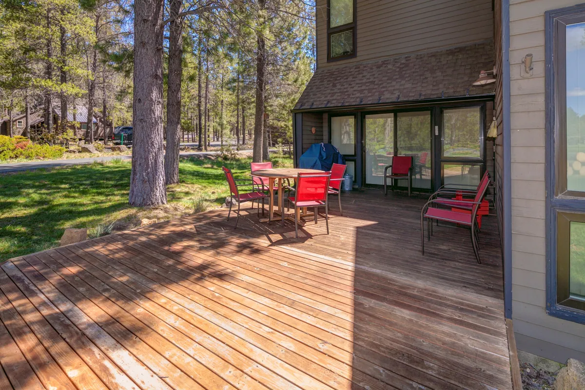A spacious wooden deck is featured with striking red chairs and a sleek glass wall, creating an inviting setting just outside the living area. The deck is arranged for outdoor dining and gatherings, and it offers clear views of the golf course, capturing both morning and evening light. The setup includes ample seating and an open-air atmosphere that welcomes both guests and pets.