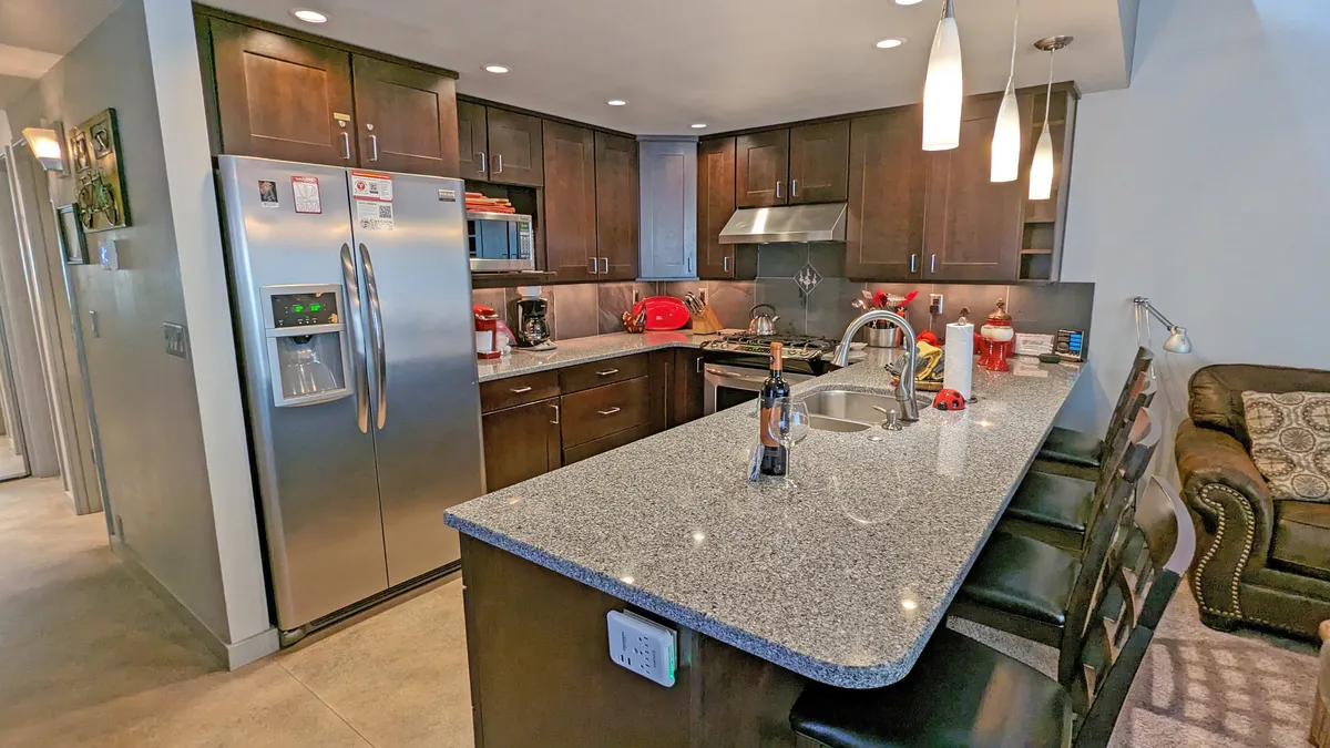 A beautifully remodeled kitchen featuring granite countertops, sleek stainless steel appliances, rich wood cabinetry, and inviting bar stools. Natural light floods the space, and signs of thoughtful touches like cookbooks and spices are visible on the counters. The open design hints at flow toward adjoining living and dining areas.