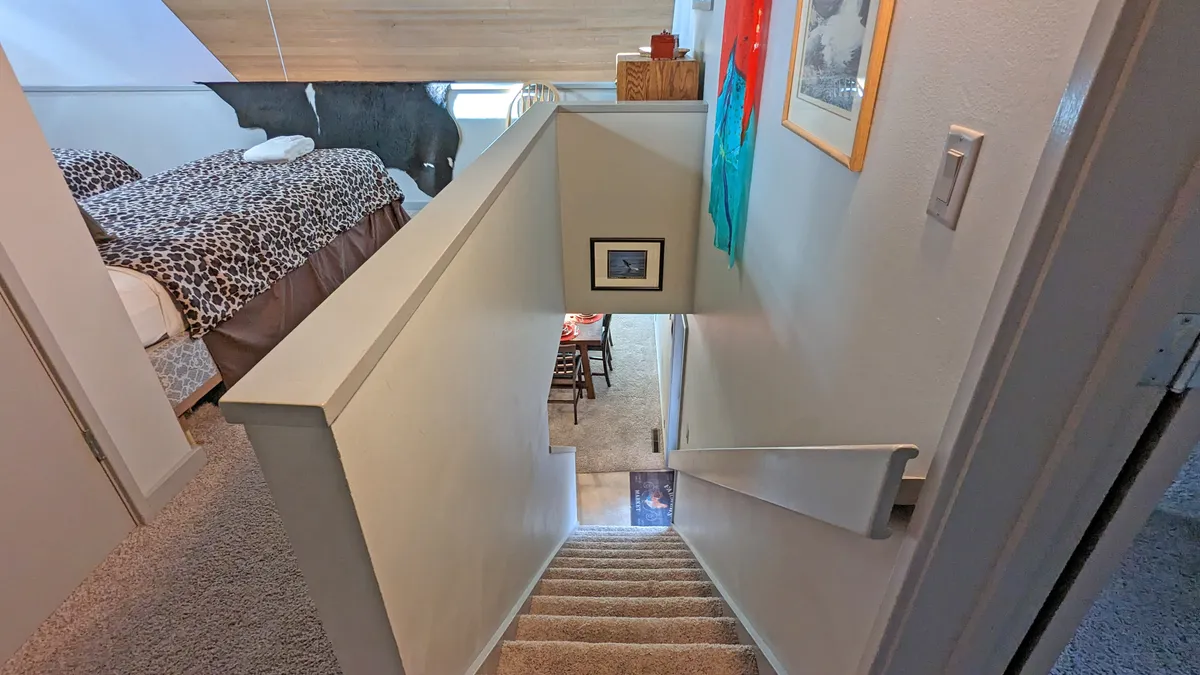 A view that blends multiple gathering spaces, featuring a staircase, a glimpse of a bedroom with distinctive bedding, colorful artwork, and, importantly, a dining area set for shared meals. The overall vibe is warm, lived-in, and inviting.