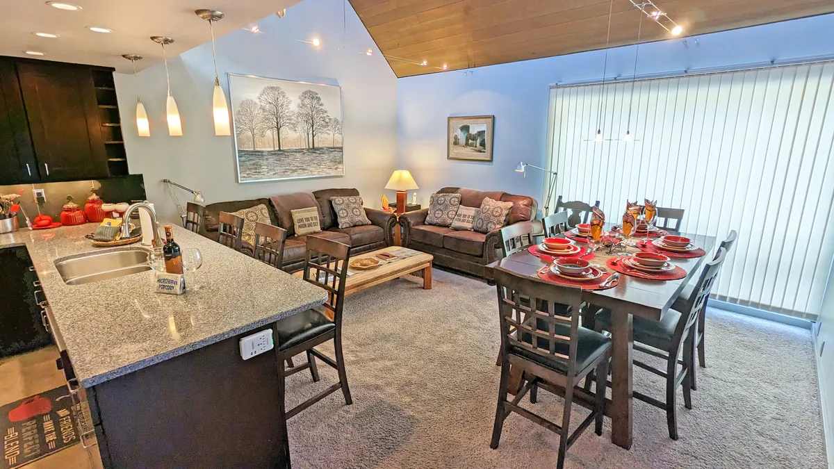 A stylish kitchen and dining area with a granite countertop, comfortable seating, a dining table set for a meal, and tasteful artwork. The space feels ready for family meals, game nights, or planning the next day’s activities.