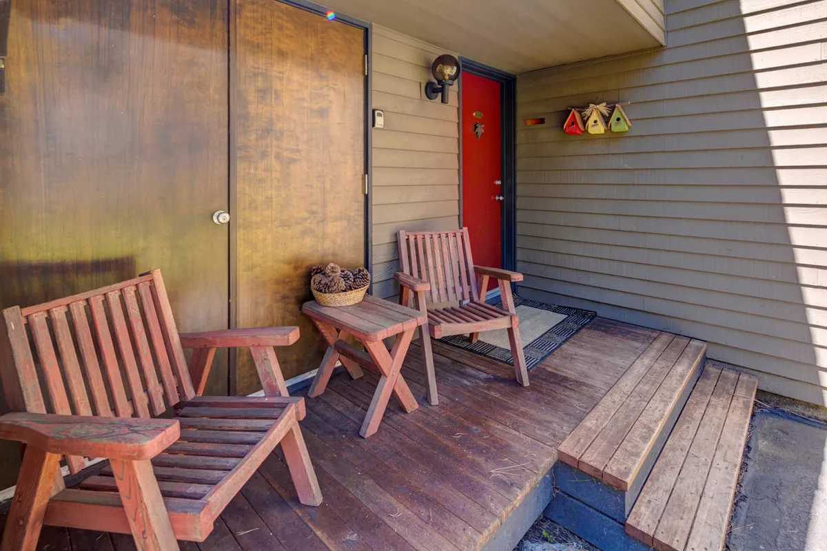 This exterior shot features a welcoming red door, wooden chairs positioned on a deck or porch area, and tasteful decorative accents. The scene gives a direct sense of outdoor living, highlighting a space designed for relaxation and socializing while taking in the surrounding environment.
