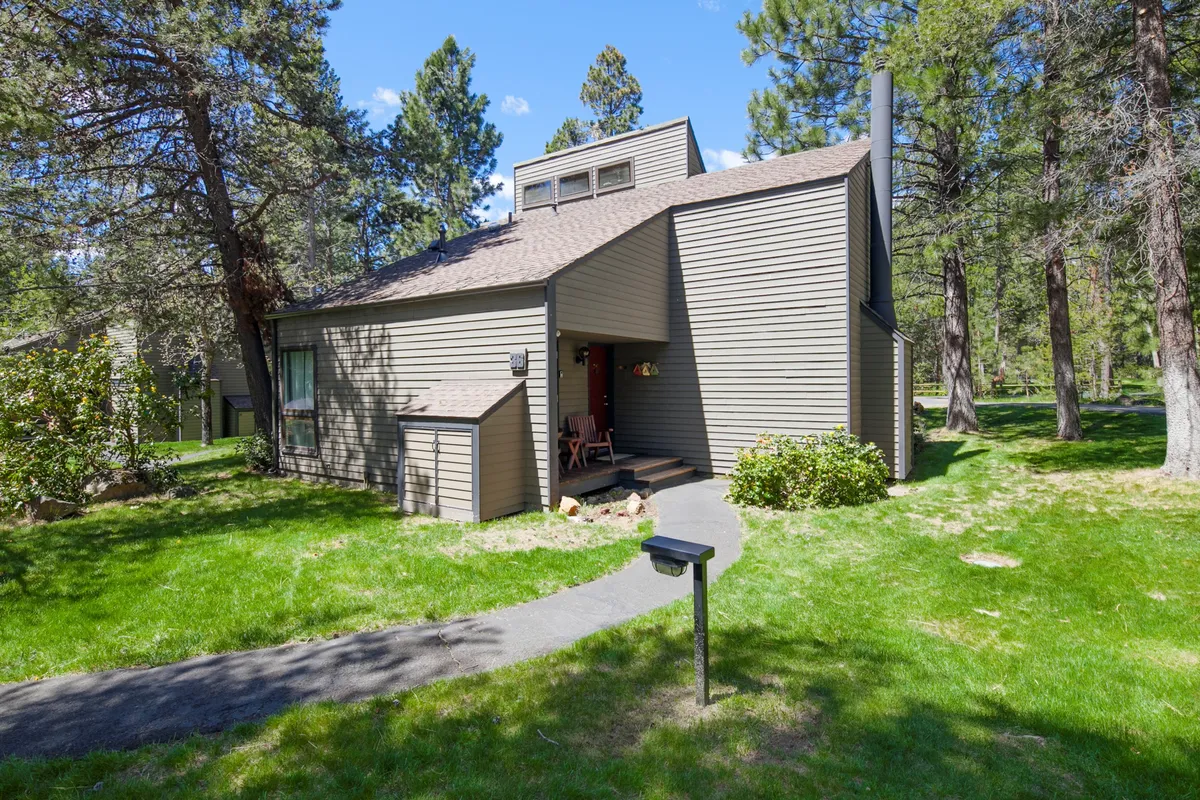 A welcoming front porch with comfortable seating, a landscaped yard, and a pathway leading into the surrounding trees. The setting suggests both relaxation and immediate access to nature and local trails.