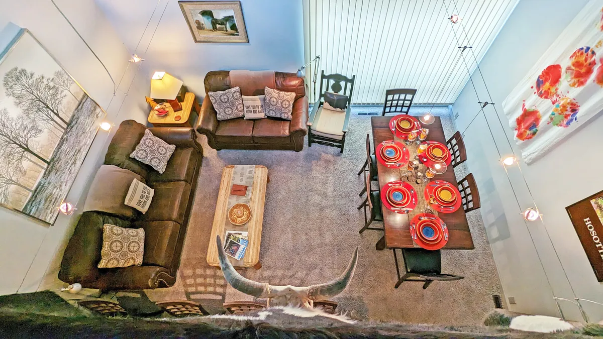 A warm dining and living space featuring cozy sofas, a dining table set with colorful plates, eye-catching artwork, and a wooden coffee table. The space is designed for socializing, casual meals, and unwinding together.